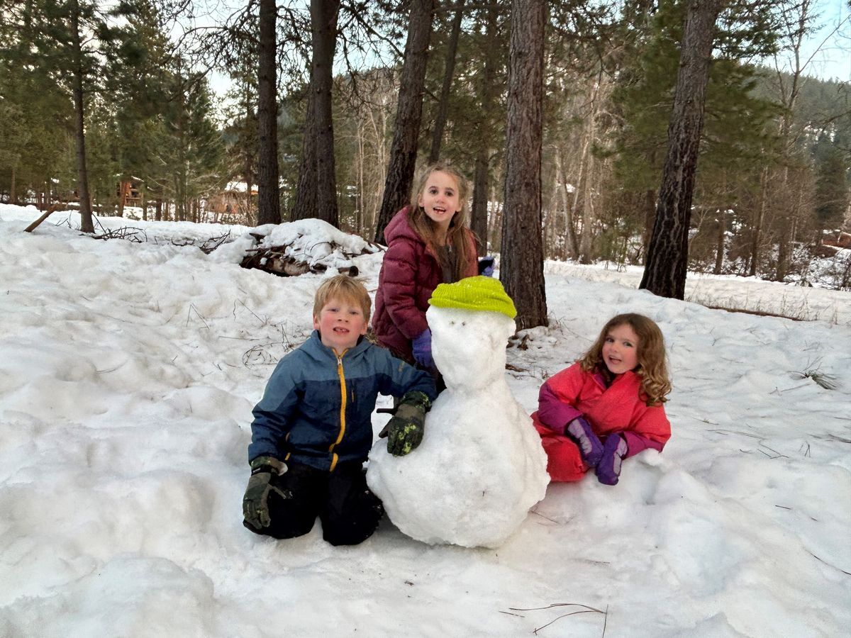 Three students posed in their snow gear next to a snowman they built together.