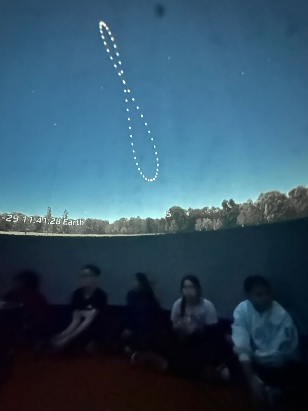 Students seated inside the planetarium looking up at the night sky constellations.