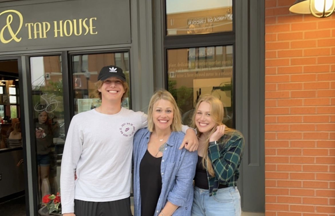 Photo of family of three outdoors. Mother in the middle between her two grown children, son on the left and daughter on the right. 