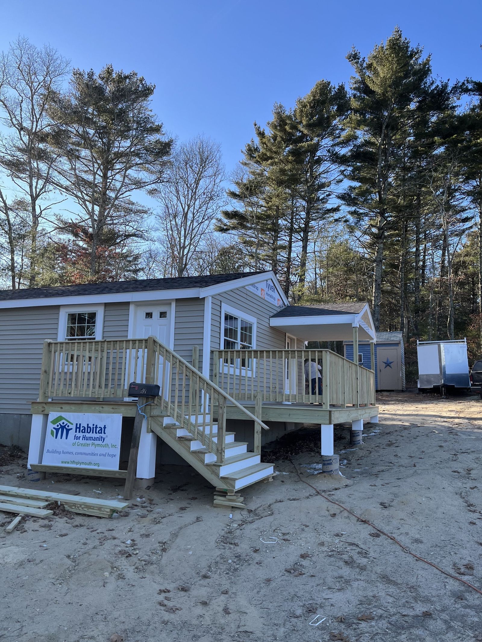 Photo of house with beige vinyl siding complete and two entryway porches, with a Habitat for Humanity sign in front