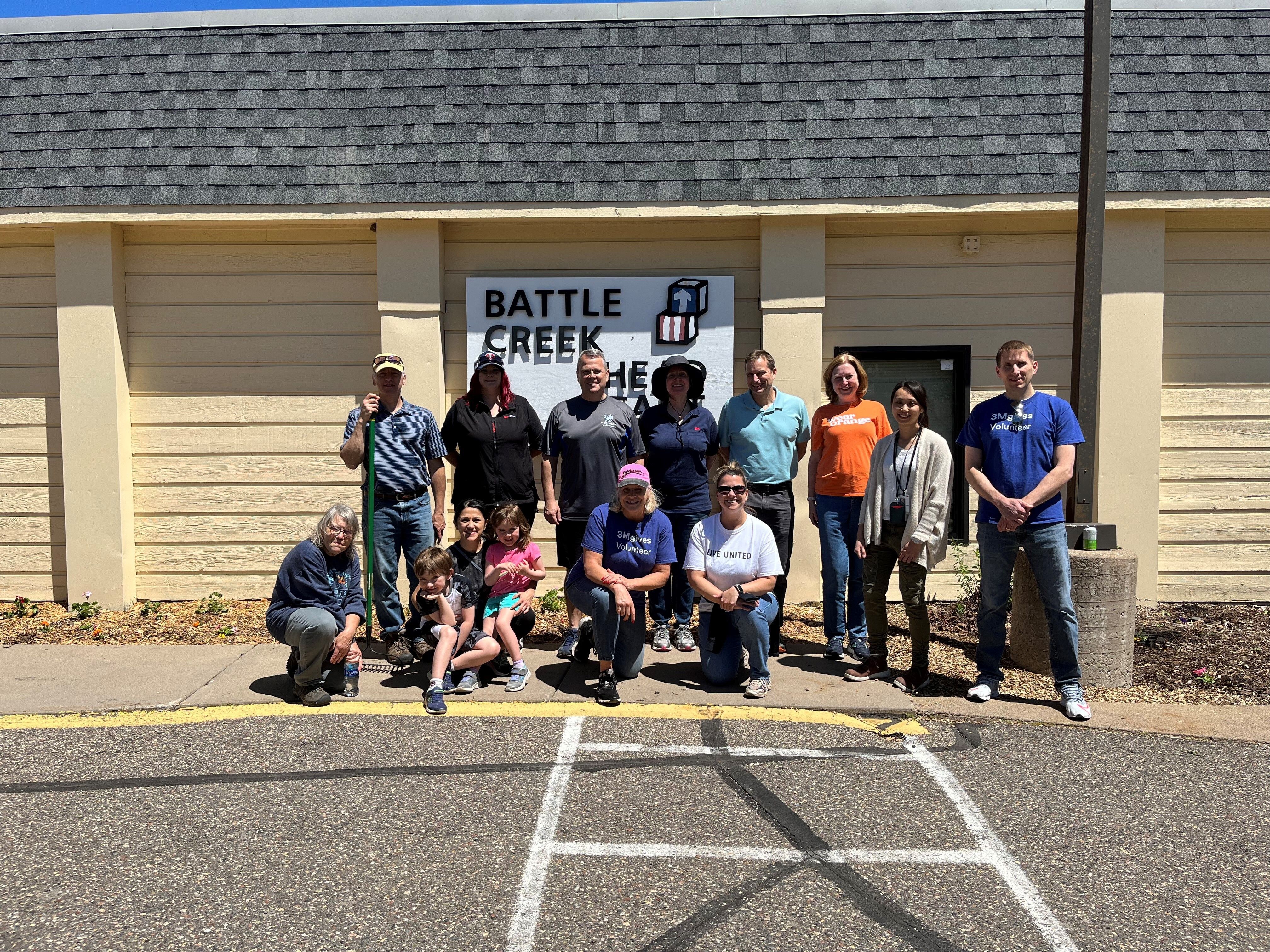 A group of people stand in front of a building smiling with gardening tools in their hands