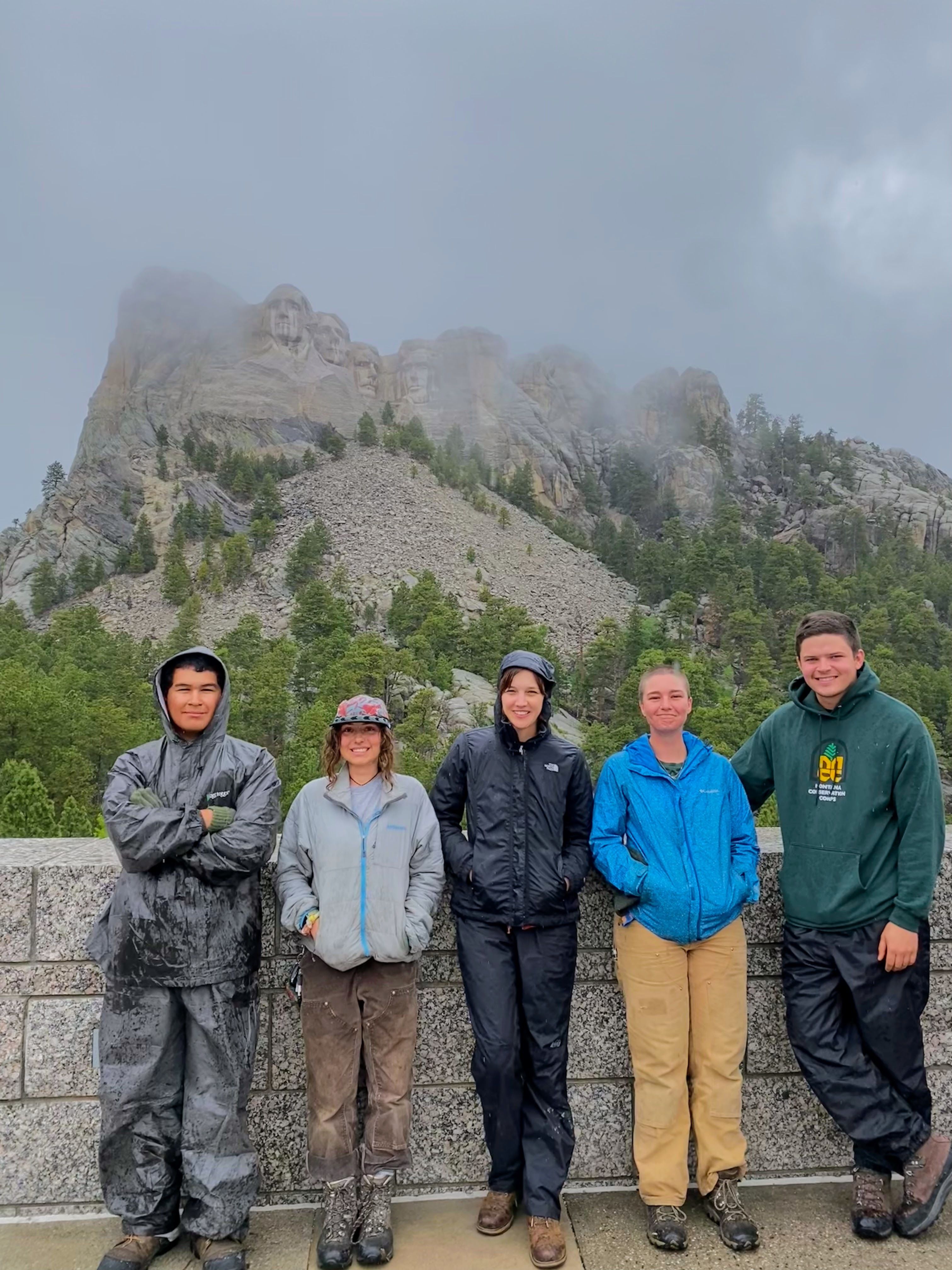 A crew poses in the rain in front of Mount Rushmore