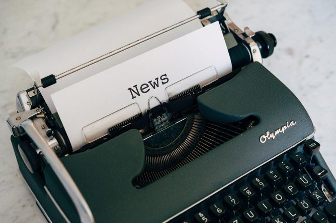A piece of paper in a typewriter with the word "News" typed across the top center.