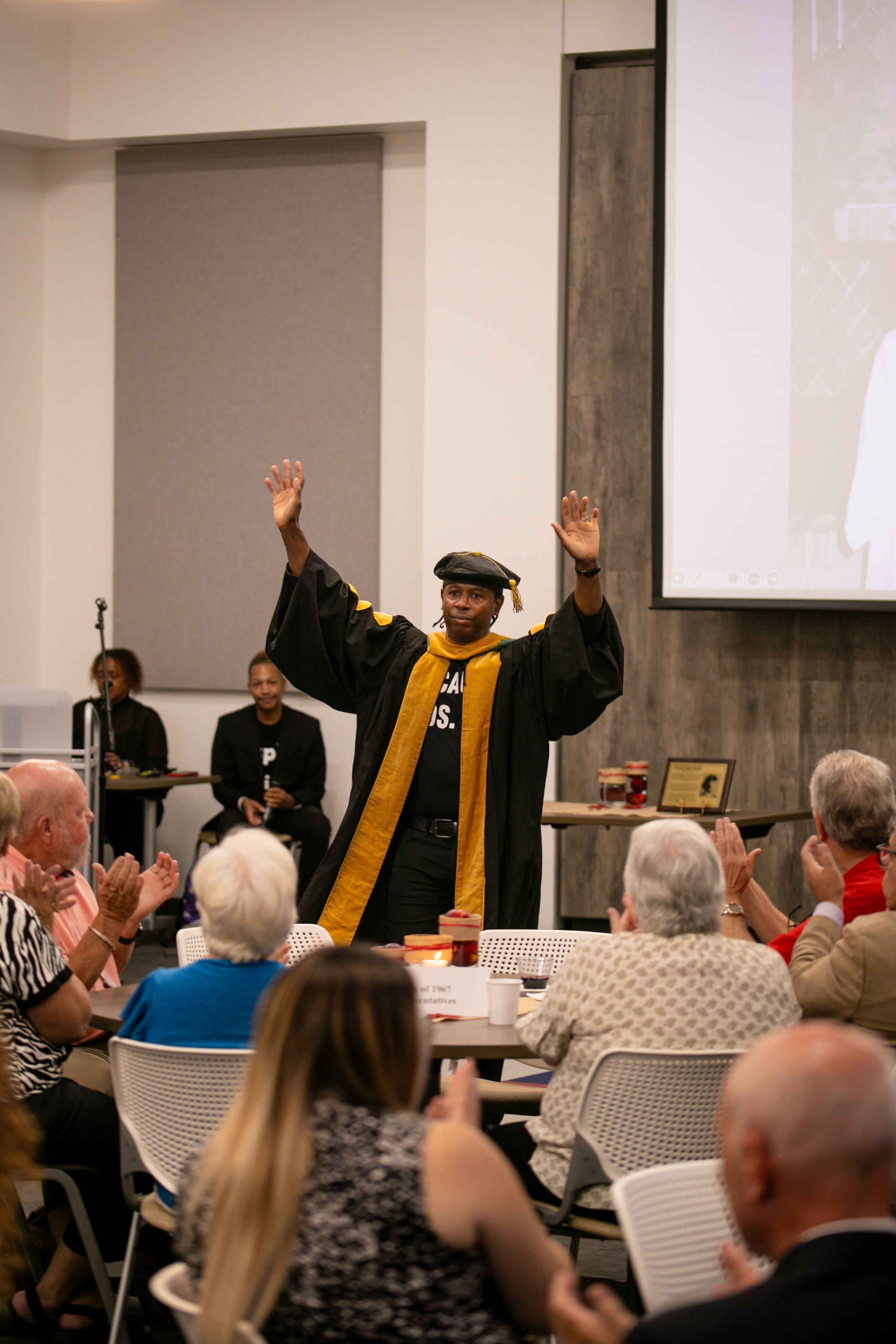 Dr. Adolph Brown, in a doctoral graduation garb, speaks to the audience. 