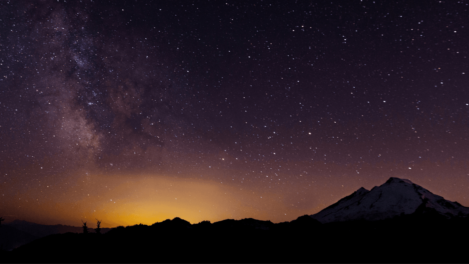 Starry night sky over mountain with sunrise beginning