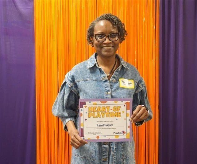 Volunteer Ms. Pam holding up her "Heart of Playtime" award.