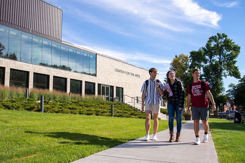 students walking in front of the Larry Robinson Center for the Arts, engaging in conversation and carrying backpacks