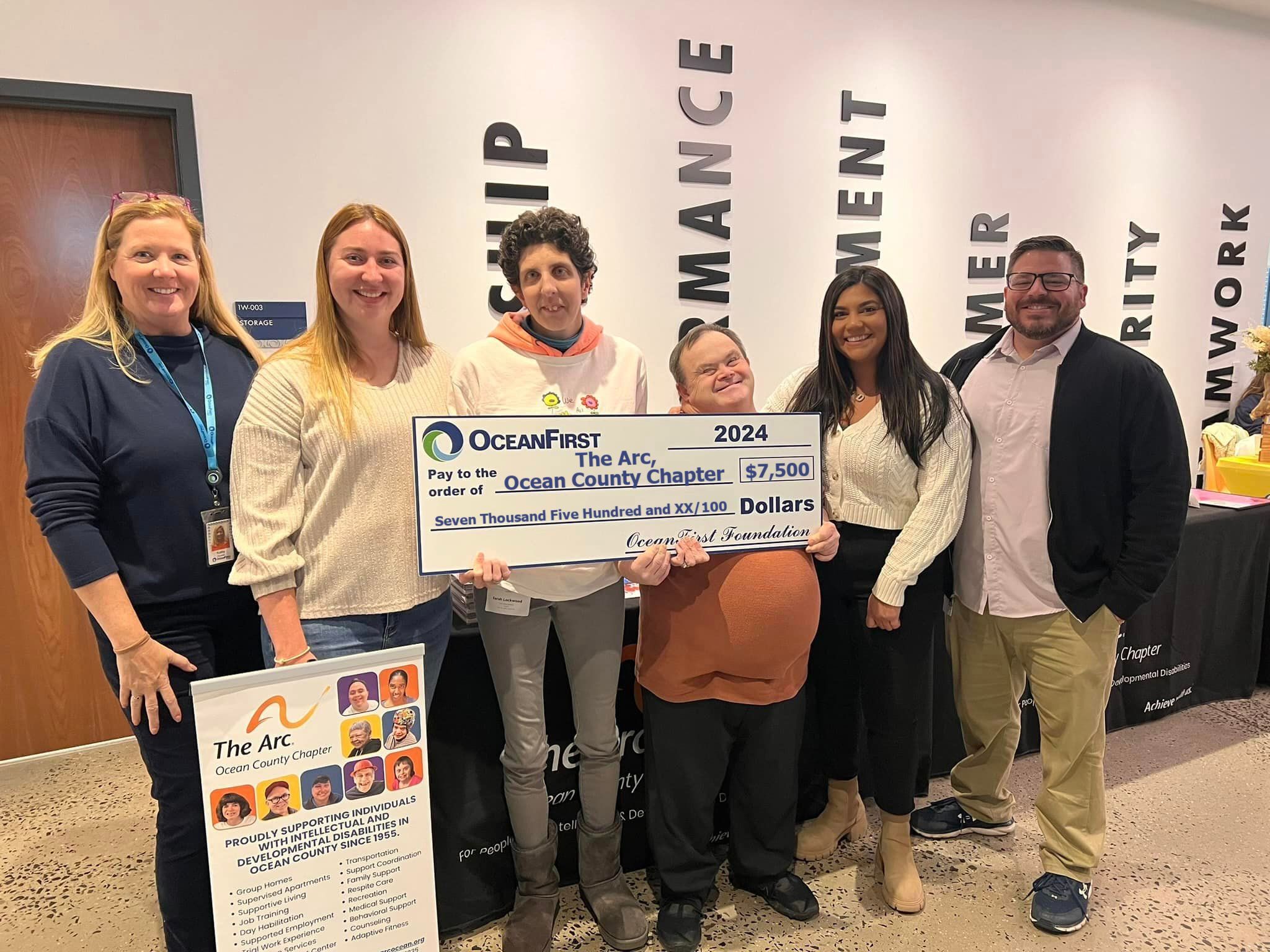 4 women and 2 men smiling while holding an oversized check.