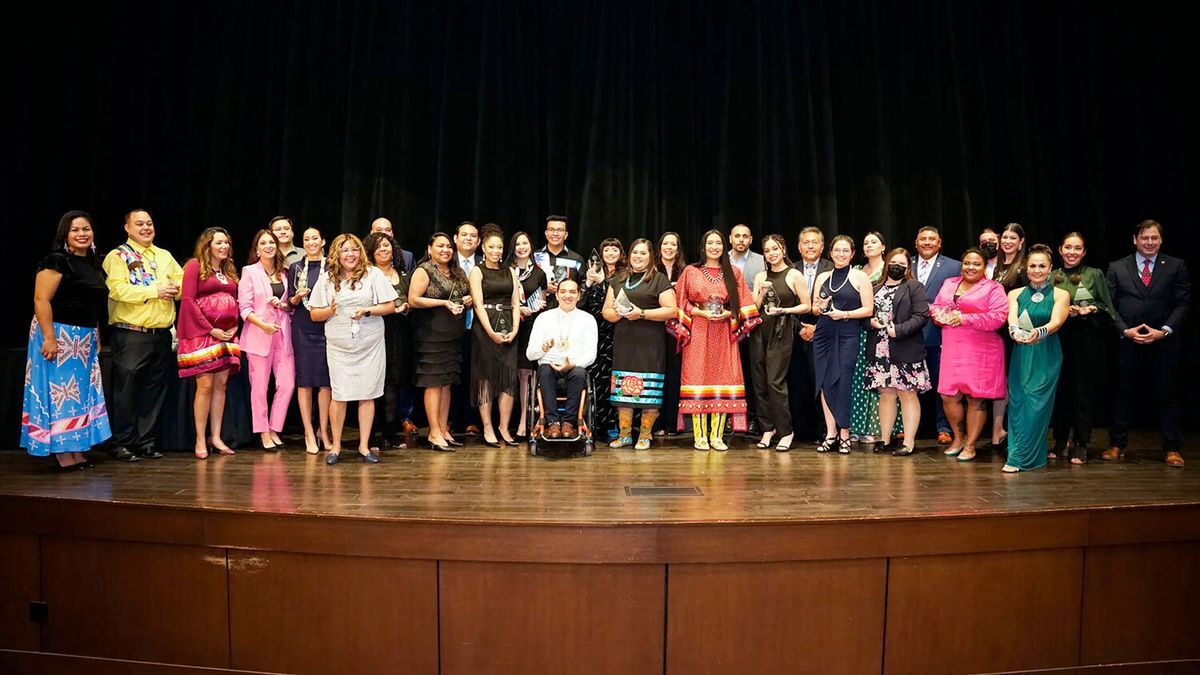 The group of 2021 40 Under 40 award winners dressed in formal attire stand on a stage, some holding 40 Under 40 awards.