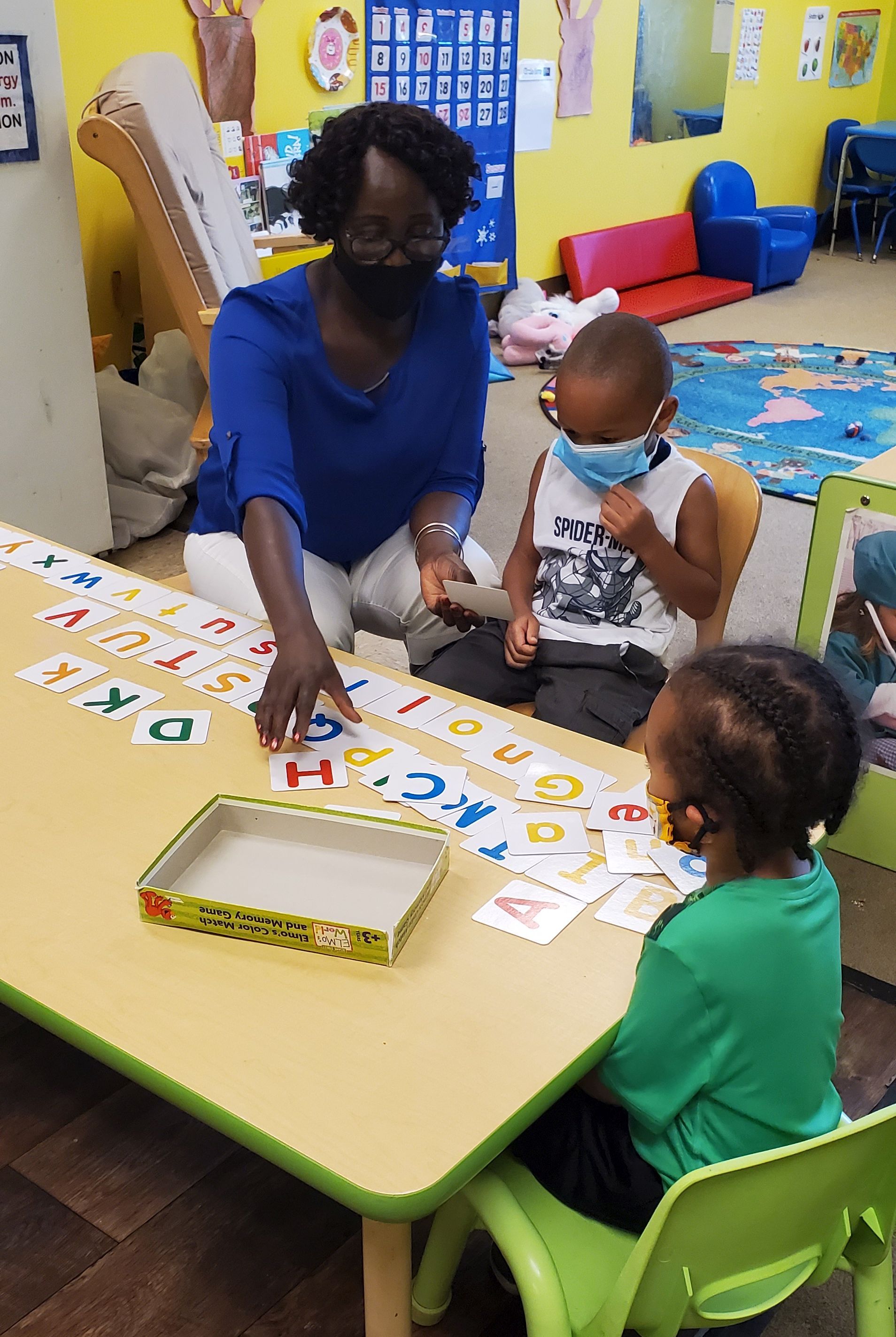 A teacher is sitting at a table with two small children and shows them flashcards with letters of the alphabet.