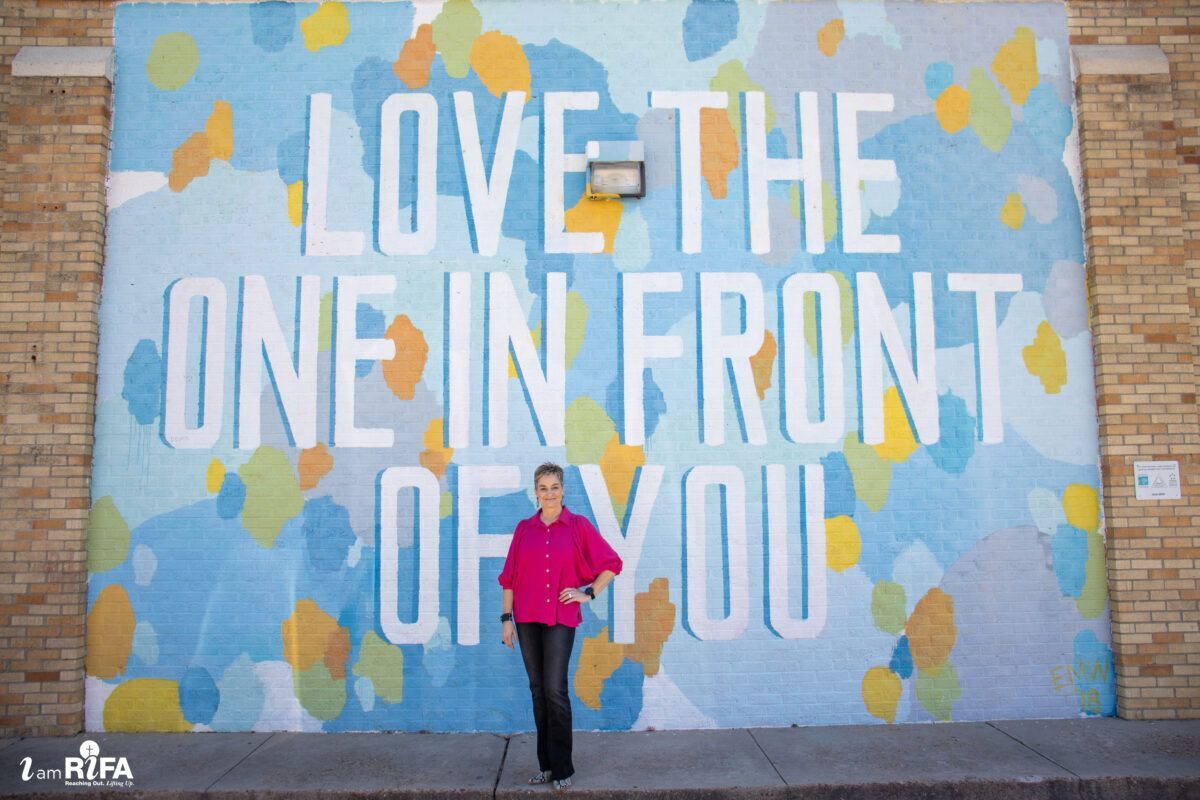 Cassandra Fuller standing in front of "Love the one in front of you" colorful mural