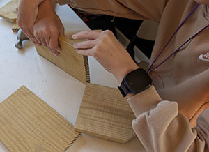 Student hands assembling wooden birdhouse pieces on a table