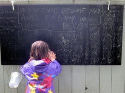 Child in a colorful raincoat looking at a chalk-covered blackboard.