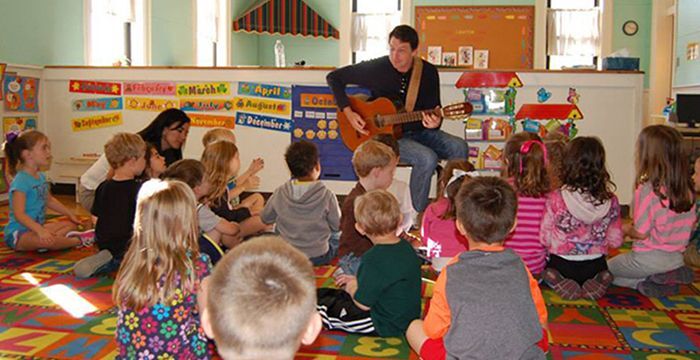Jason Riley playing guitar to kids at school.