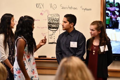 4 students presenting a compelling project on "Water Sanitation" at a whiteboard during the World Affairs Challenge