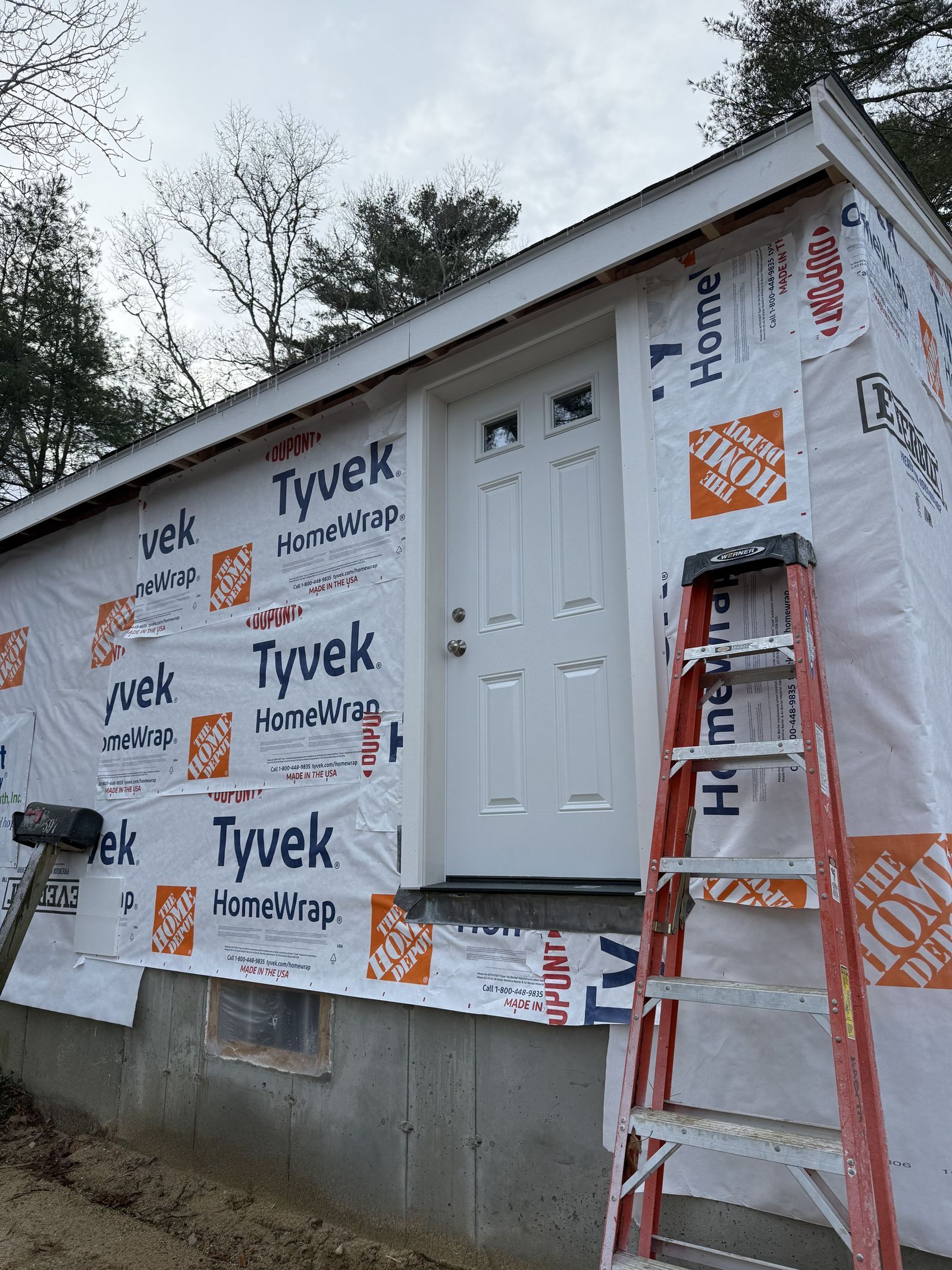 Photo of exterior of house showing a new white front door with ladder next to it