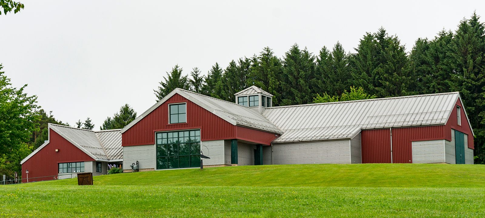 Photograph of a large building with red and metal roof and siding above a grassy hill.