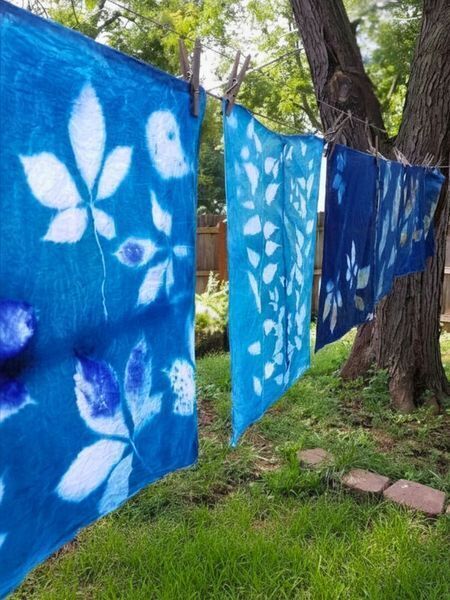 Blue bandanas with white leaf designs, hanging on a clothesline in a backyard. 