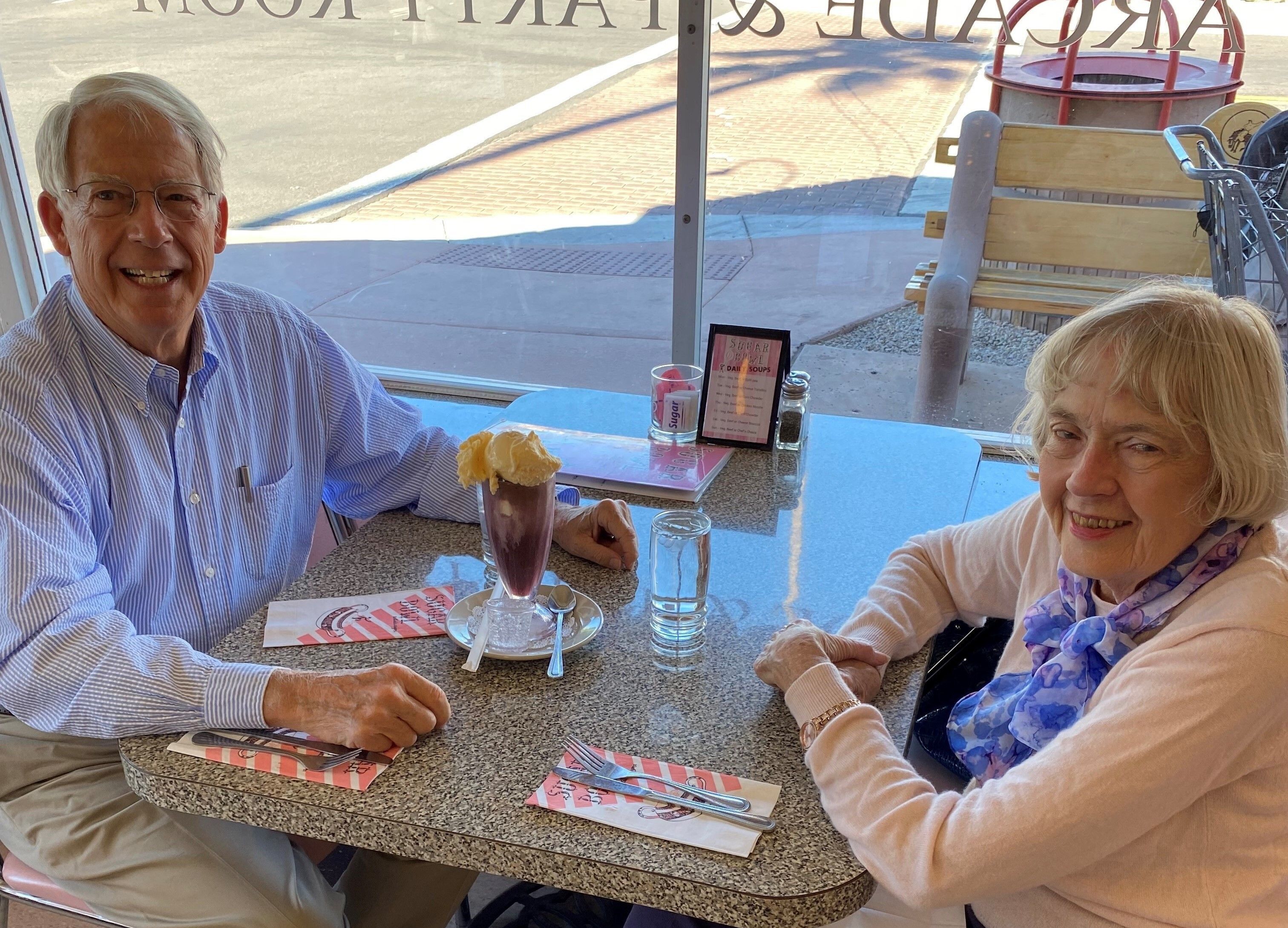 Older man sitting across from an older woman at a cafe table in an ice cream shop.