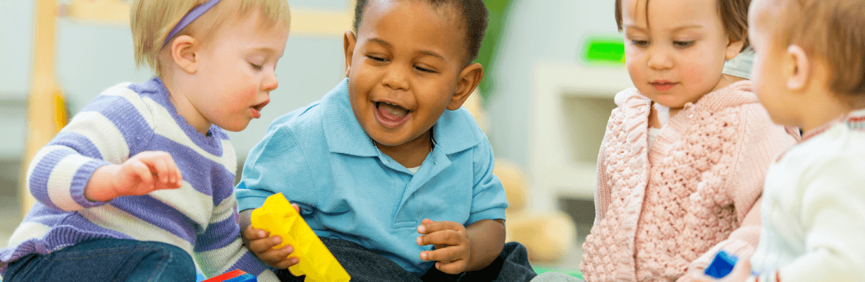 Three early intervention children sit in a playroom engaging with toys and interacting with eachother.