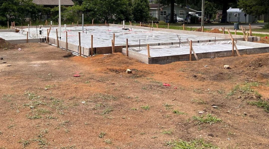 Freshly poured concrete slab foundation for a new Habitat for Humanity home, framed with wooden forms and surrounded by construction stakes