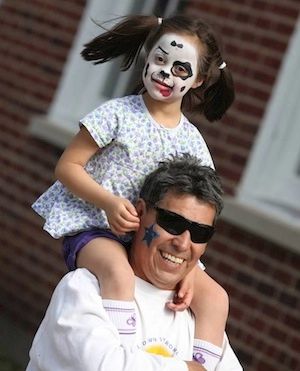 Girl child on her dad's shoulders at a past Buddy Walk for Down syndrome event.