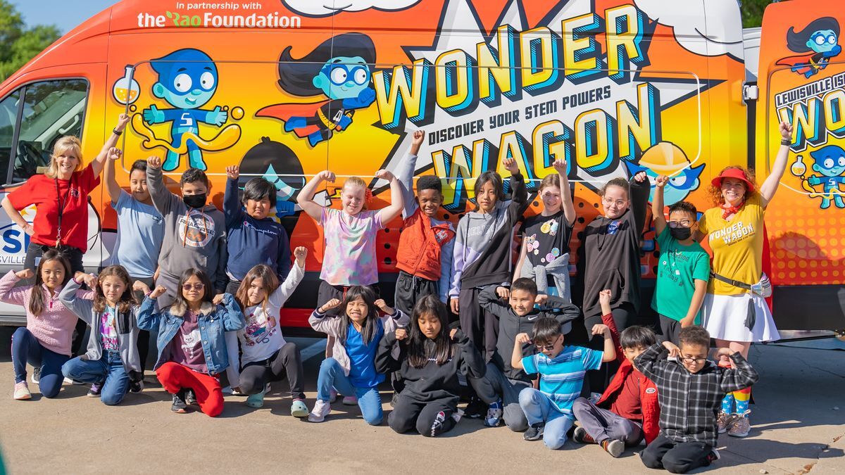 a wrapped utility van called the Wonder Wagon in the background and students and teachers smiling in front