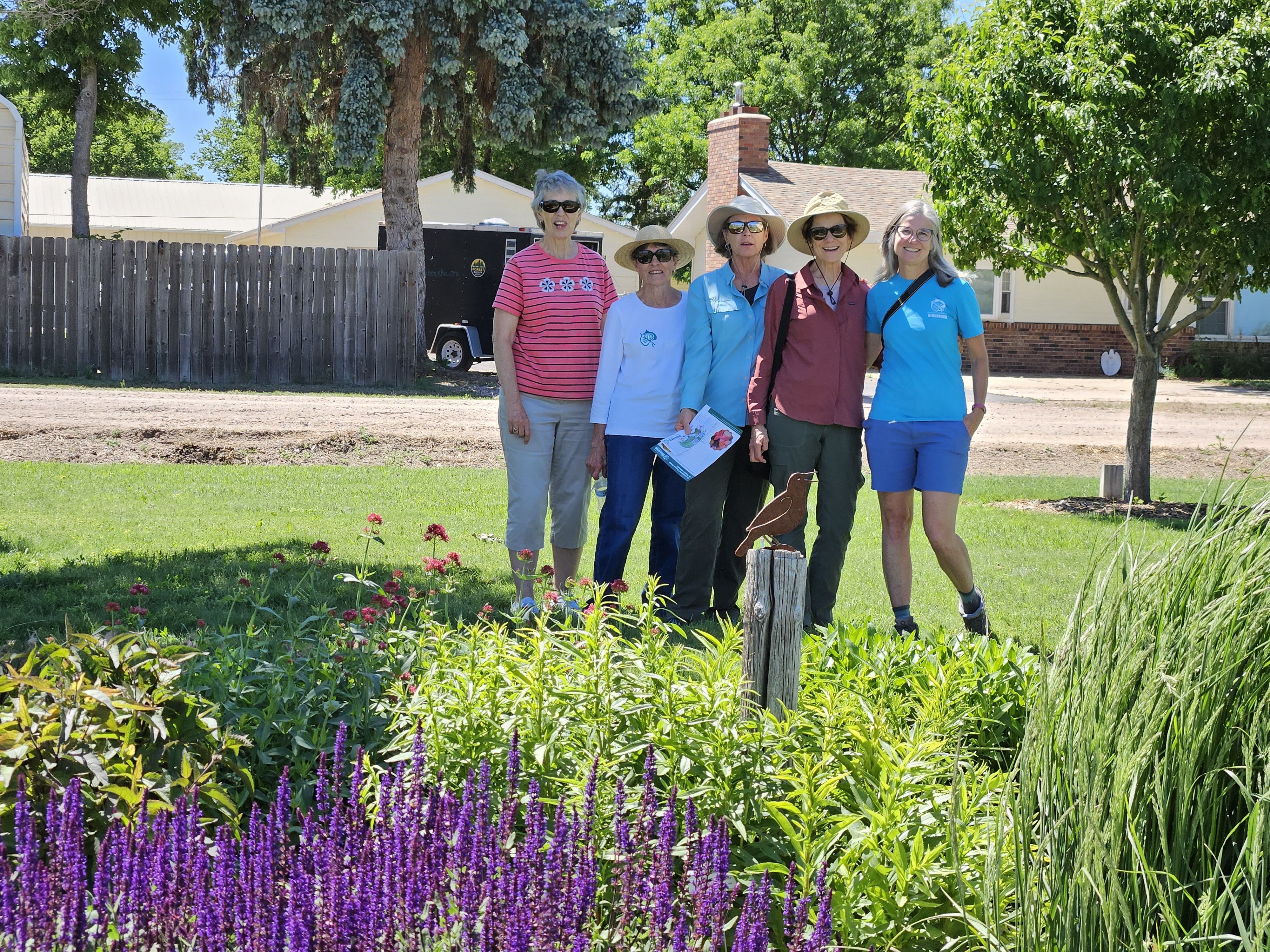 A group of women stand in a garden setting with houses in the background