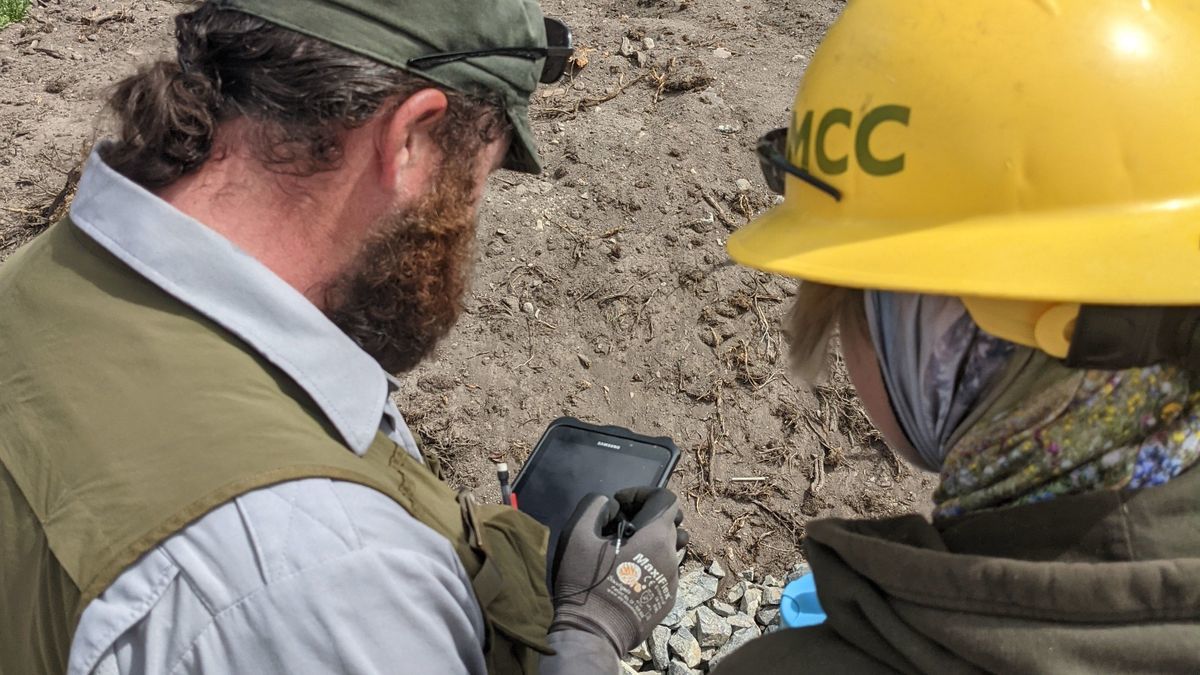 [Image Description: Two MCC members are seen viewing down on a tablet at a work site.]