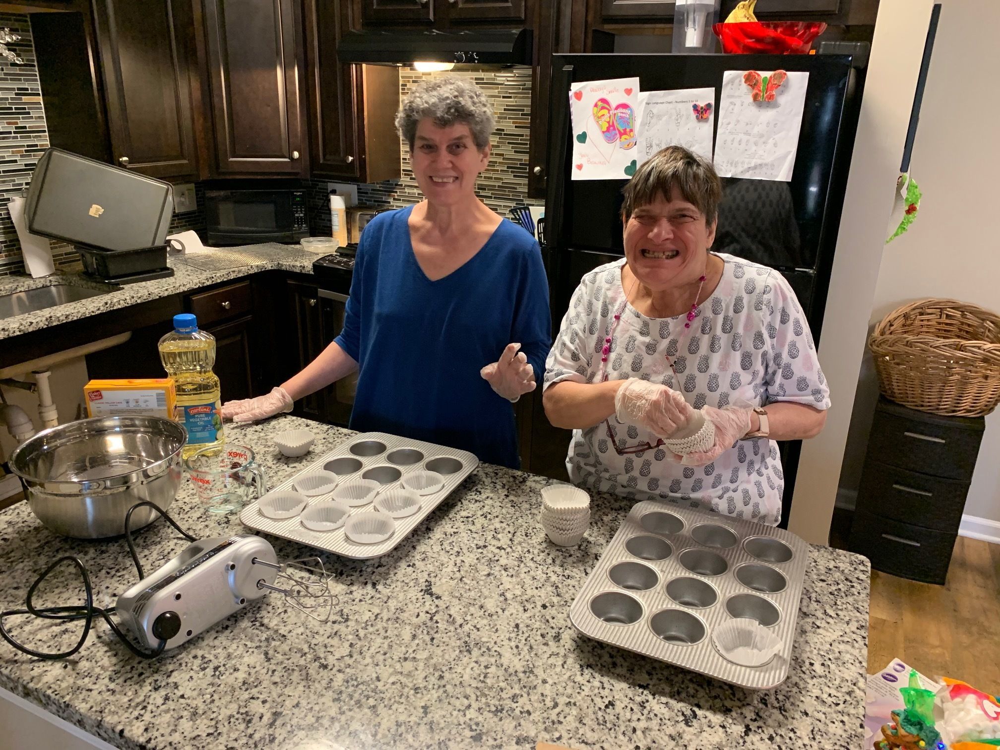 Photo of two smiling women baking cupcakes in kitchen. 