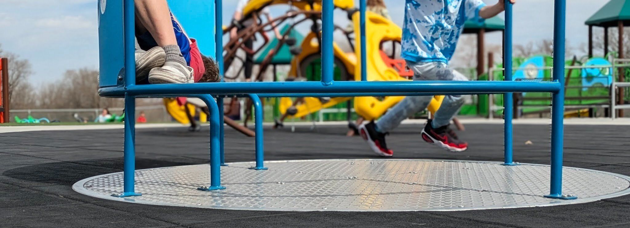 Children play on ground-level merry-go-rounds at Mahoney Inclusive Playground