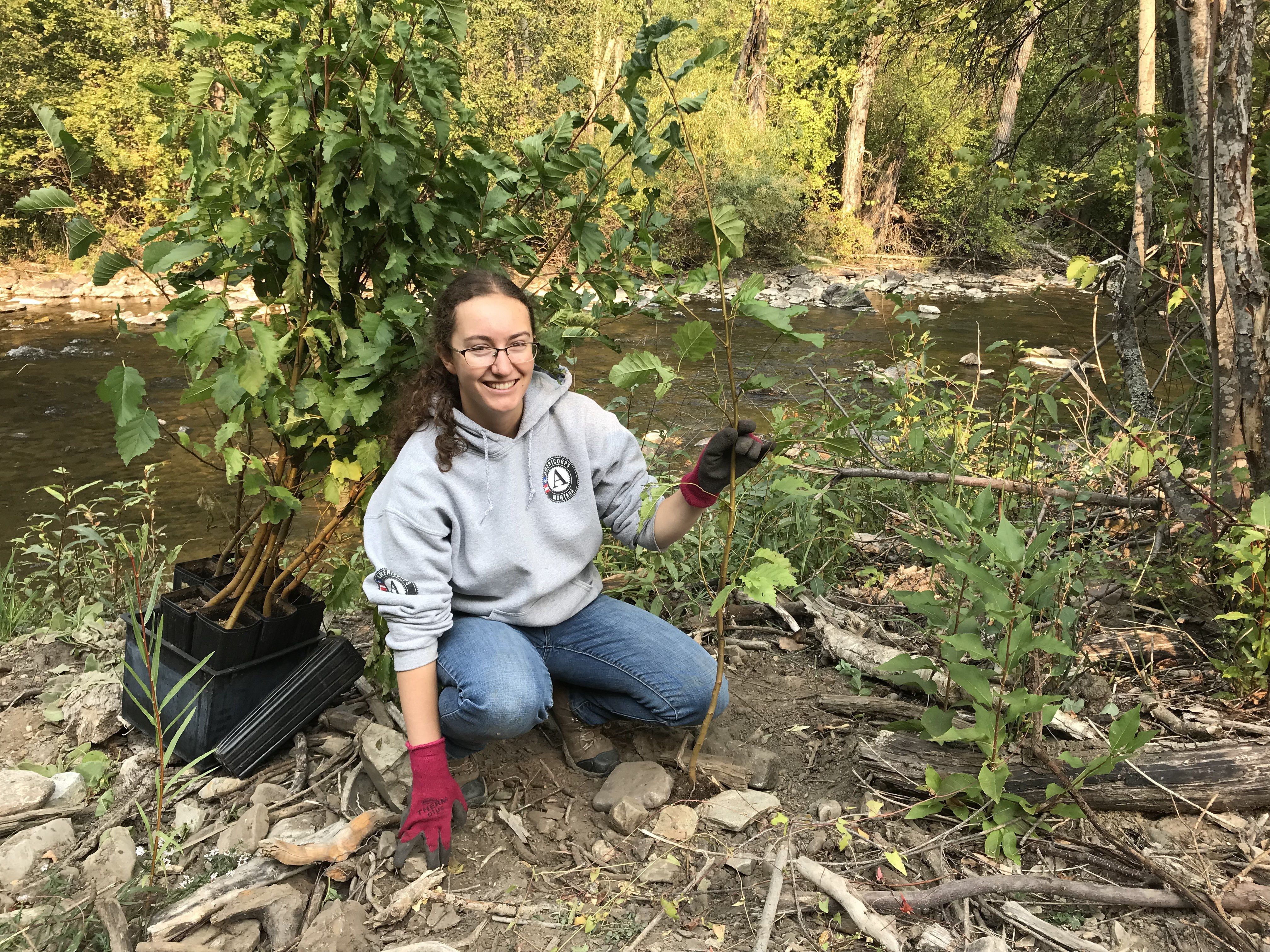 A big sky watershed corps member poses with a tree that she is planting.