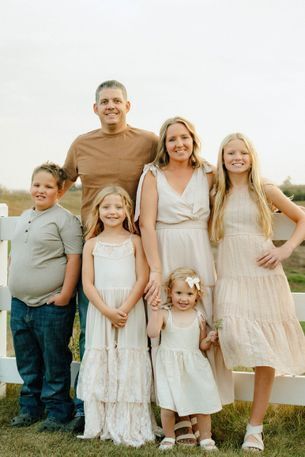 Family photo of Briggs, dad Ross, Bella, mom Amber, Braya and Brecka, standing by a fence. Farmland surrounds them