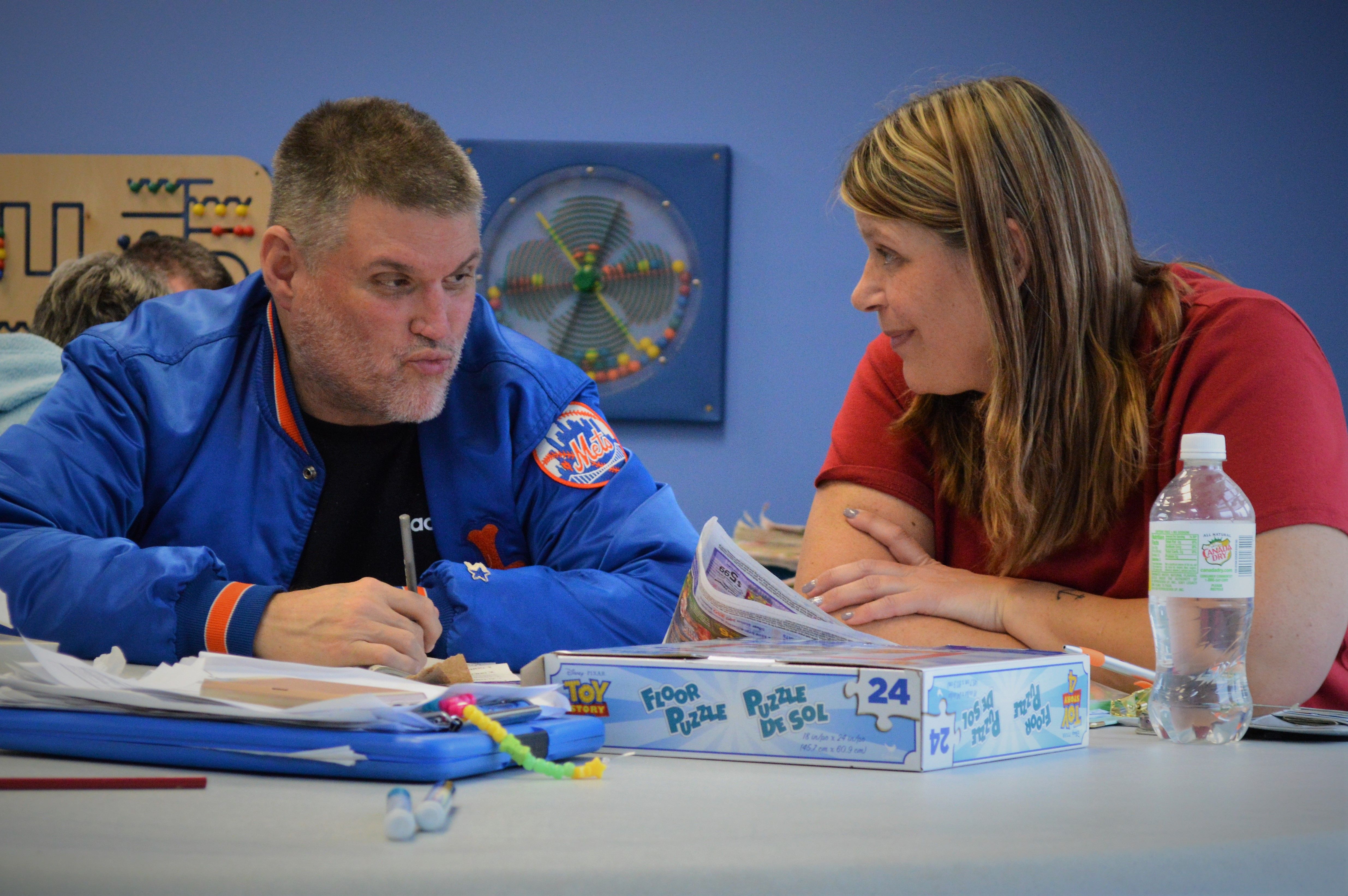 Photo of man in blue jacket and woman in red shirt talking to each other.