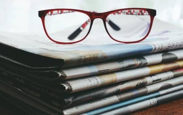 Photo of a stack of folded newspapers with red, horn rimmed glasses perched on top.