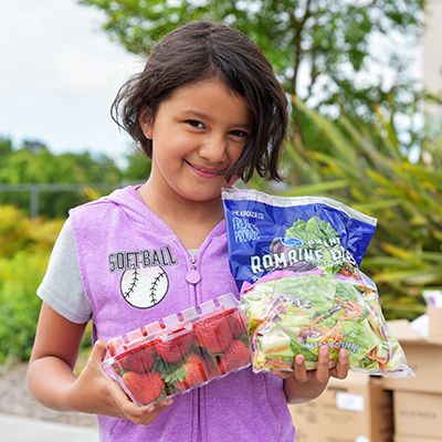 Young girl with a big smile holding strawberries and mixed lettuce