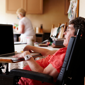 Woman in wheelchair using laptop with PCA in kitchen