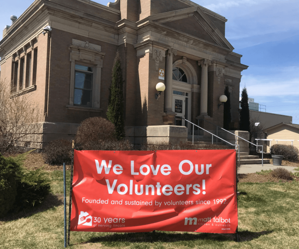 A bright orange banner outside the facility with the words "We Love Our Volunteers".
