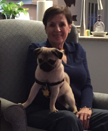 Mary O'Brien sitting in a chair, smiling and holding the pug, Luna.