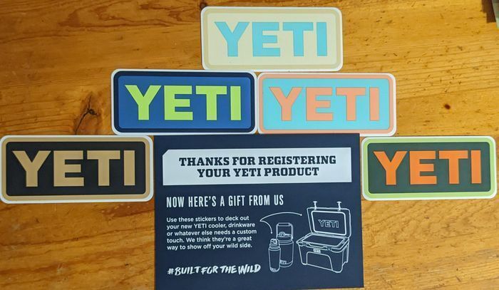 Five colorful YETI logo stickers beside a registration thank-you card, showing a sticker marketing strategy built around loyalty gifts.