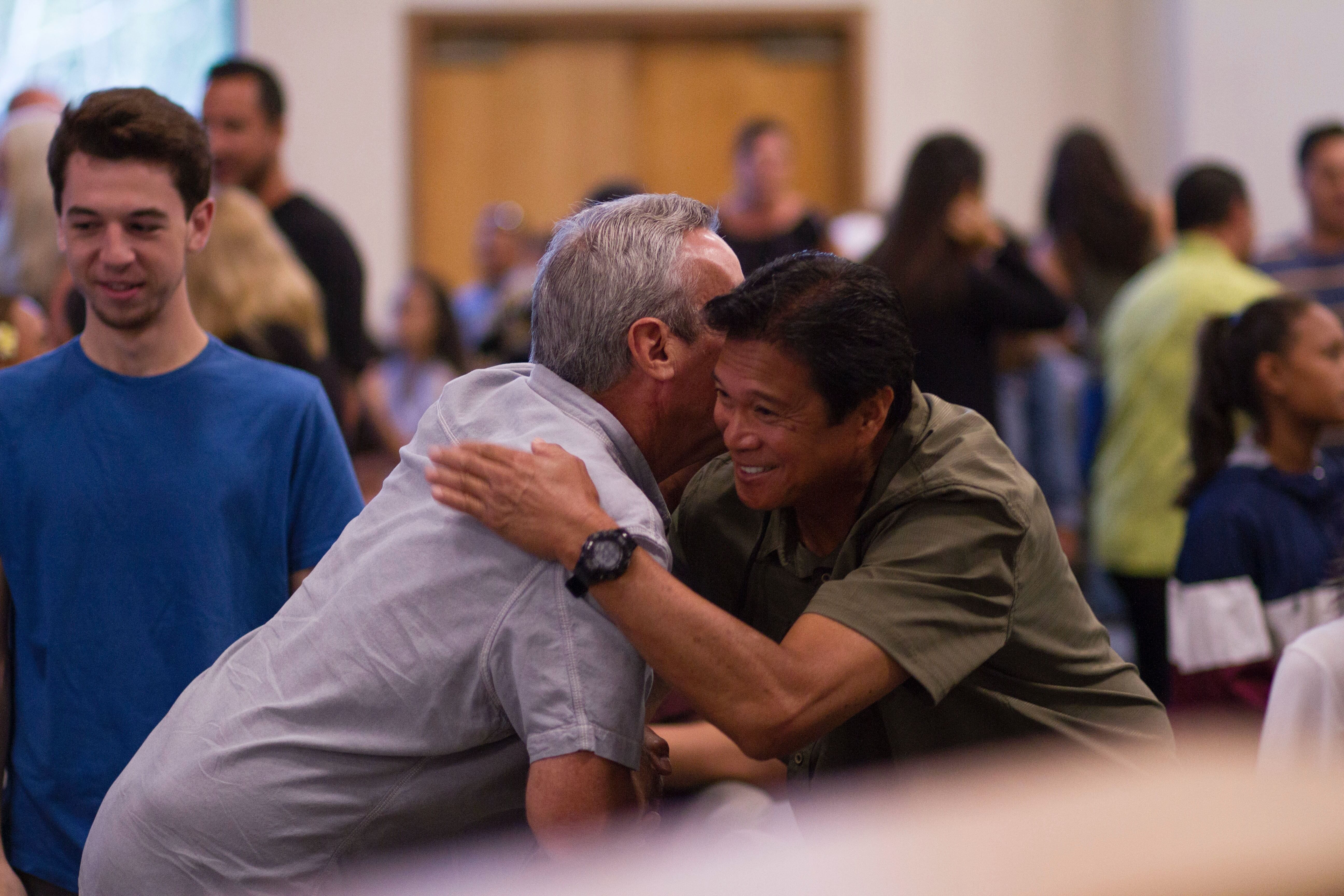 Two people at a conference embracing, one is an older man with white hair, the other is a younger asian man