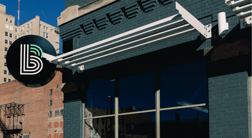 A mentor and mentee from Big Brothers Big Sisters sit together at a table, smiling as they work on a laptop. The mentee writes in a notebook while the mentor guides her, showing collaboration and learning in a bright, modern space.