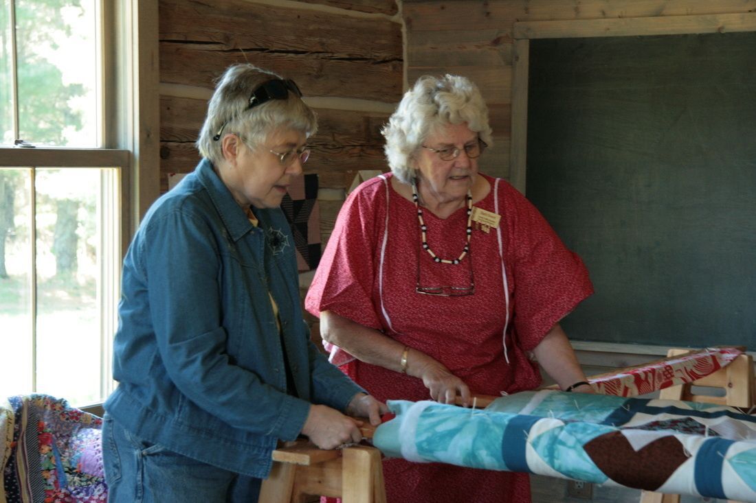 Two elderly women working on a quilt in a wood-paneled room.