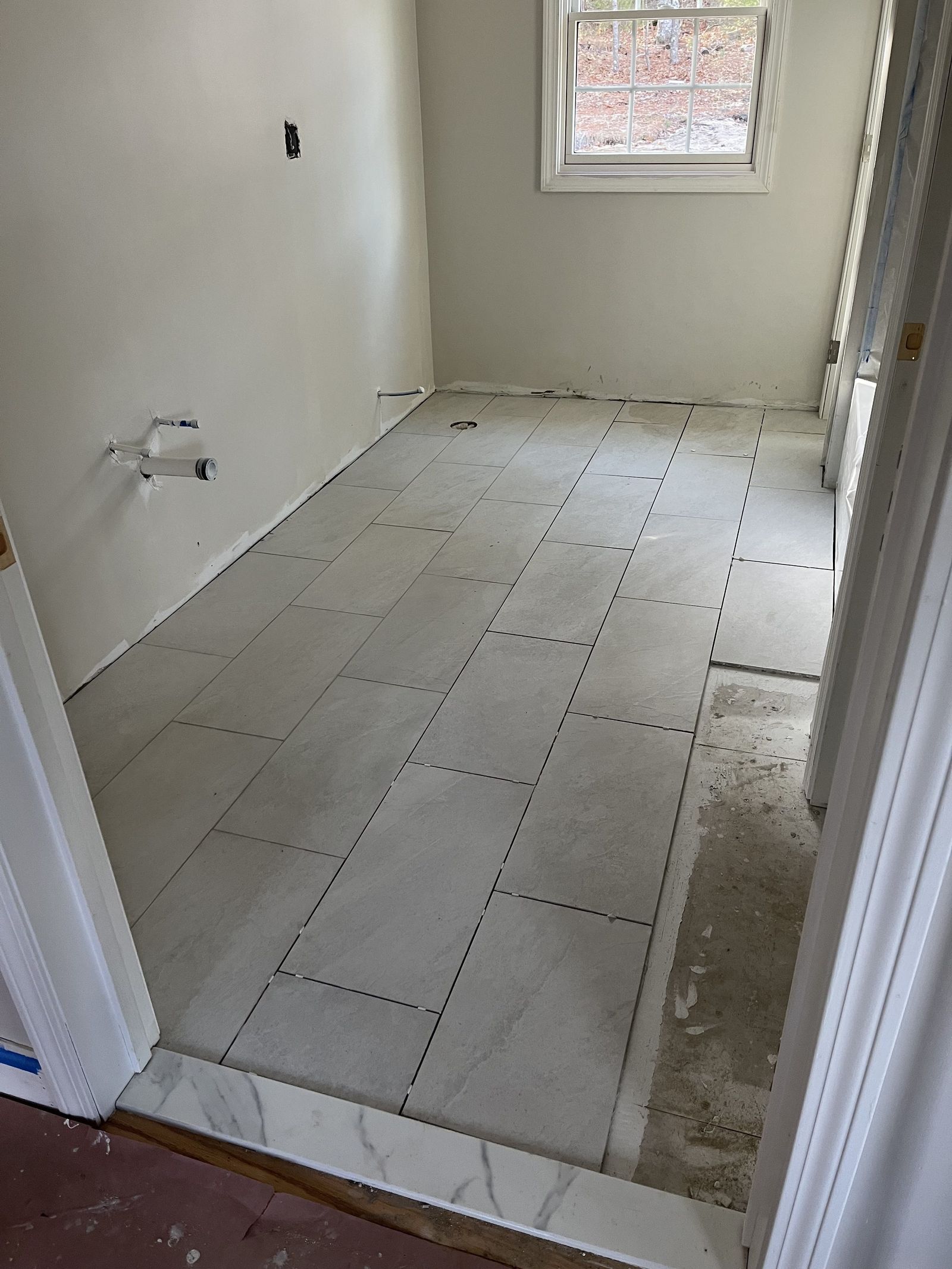 A photo of a bathroom floor with grey tile being installed