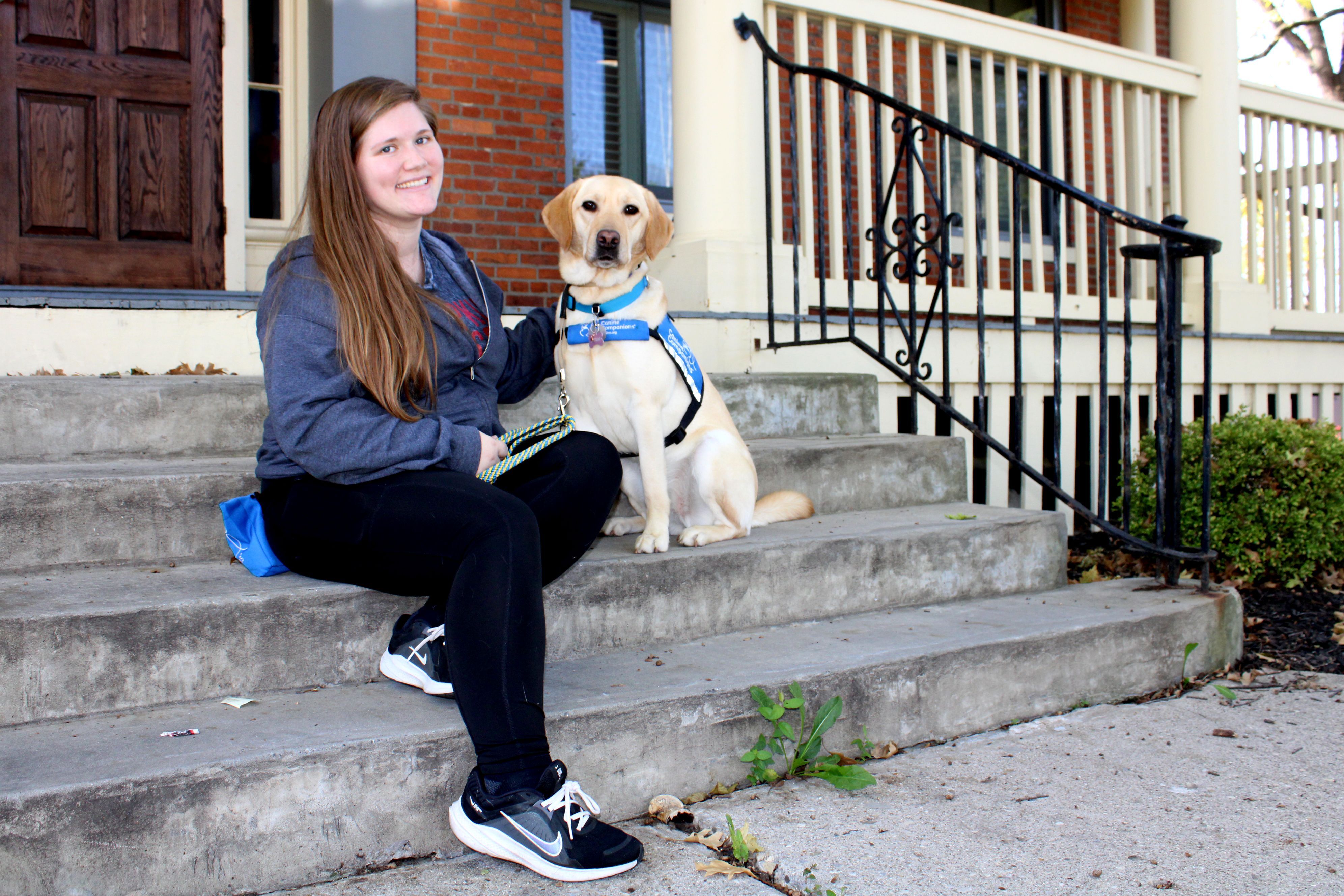 Canine Companions facility dog Tatum sits in front of the Home for Families office with plush stuffed animals from Canine Companions