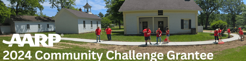 Volunteers in red shirts raking and shoveling around a sidewalk. 