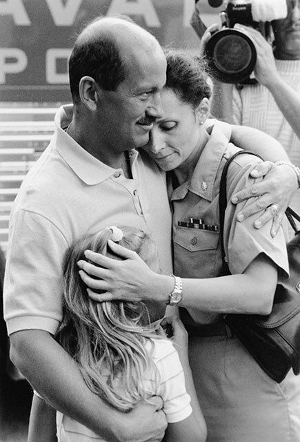 A heartfelt reunion between a man, a woman in military uniform, and a young girl.