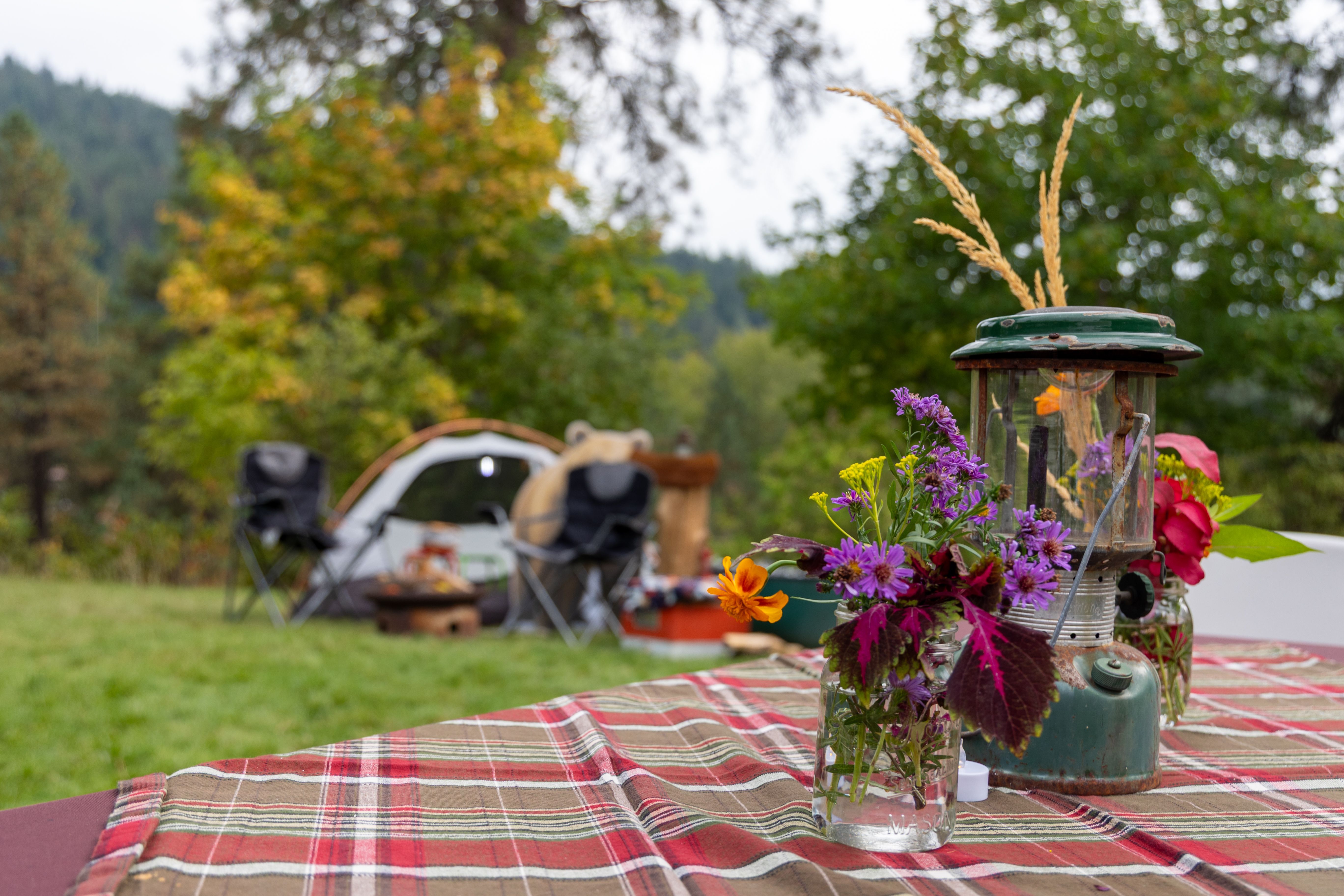 Floral arrangements and an old camping lantern on a table set for Sunset & S'mores.