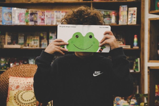 BookFace photograph of a child with an open book illustration of a frog as their face.