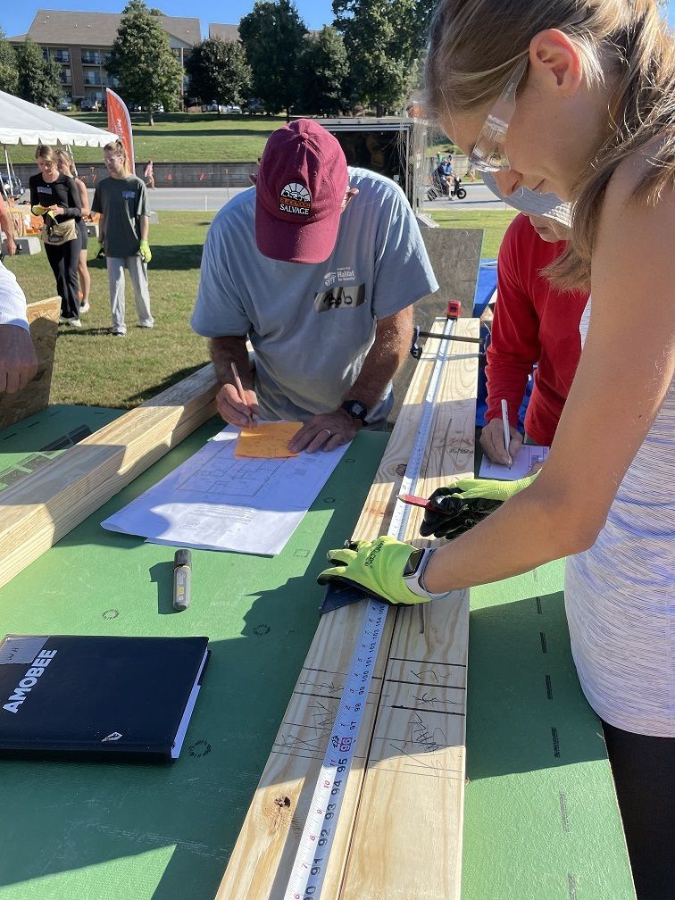 Volunteer Roxie Ware measures a board with other volunteers at the Homecoming Build